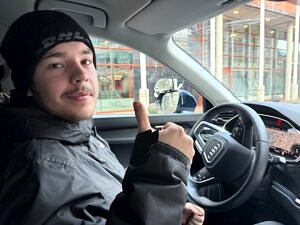 Geslaagde leerling met duim omhoog achter het stuur van de lesauto